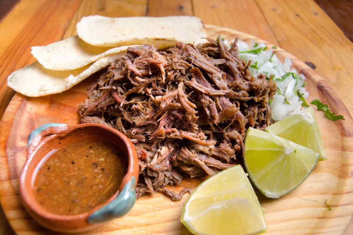 barbacoa de res servida en un plato con consomé y tortillas