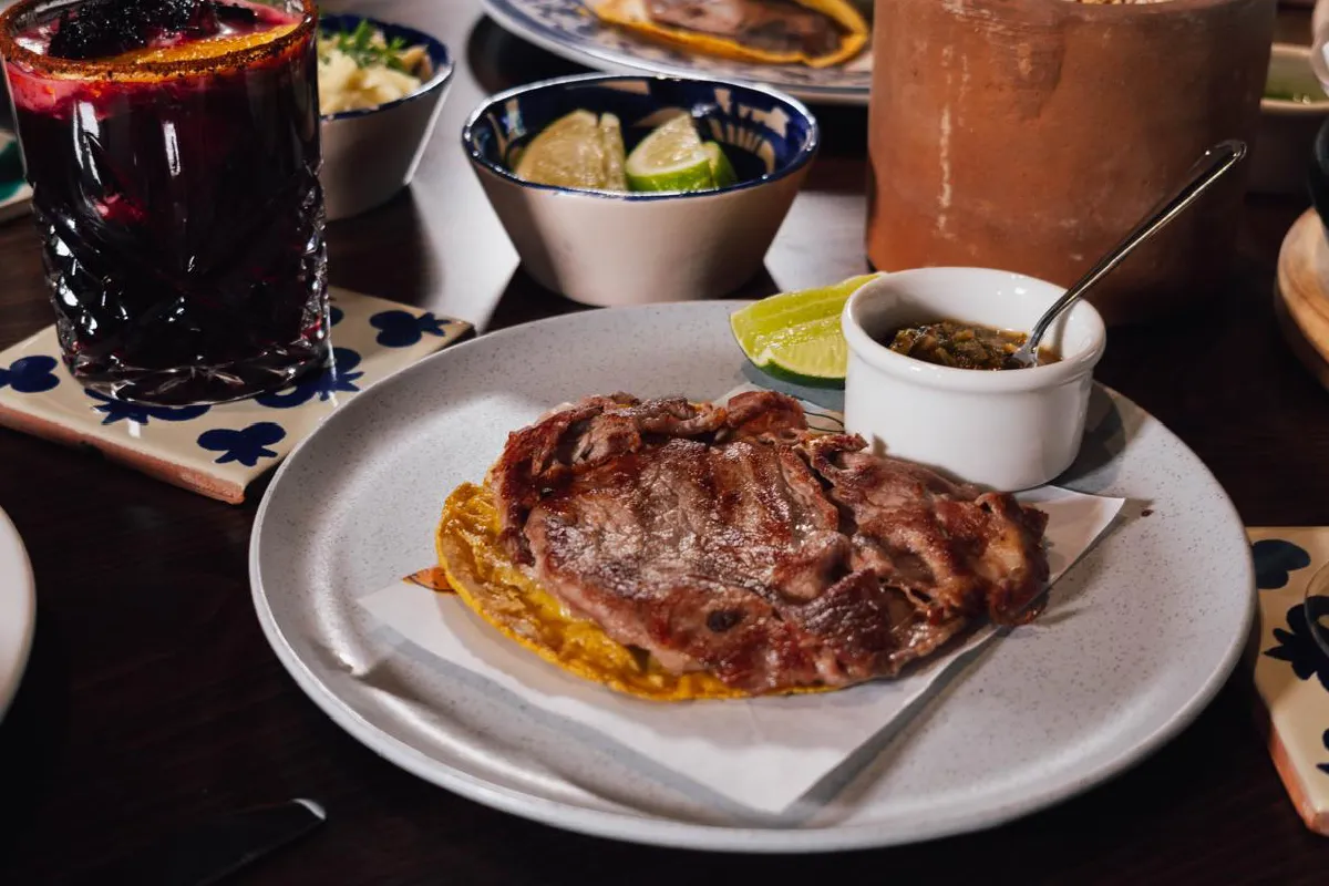 Sobre un plato blanco está una pedazo de carne con tortilla y salsa