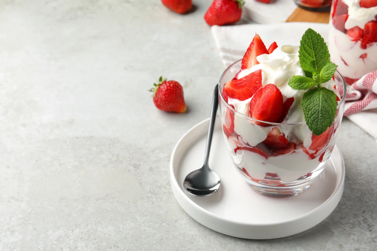 Deliciosas fresas con crema batida servidas en una mesa gris claro.