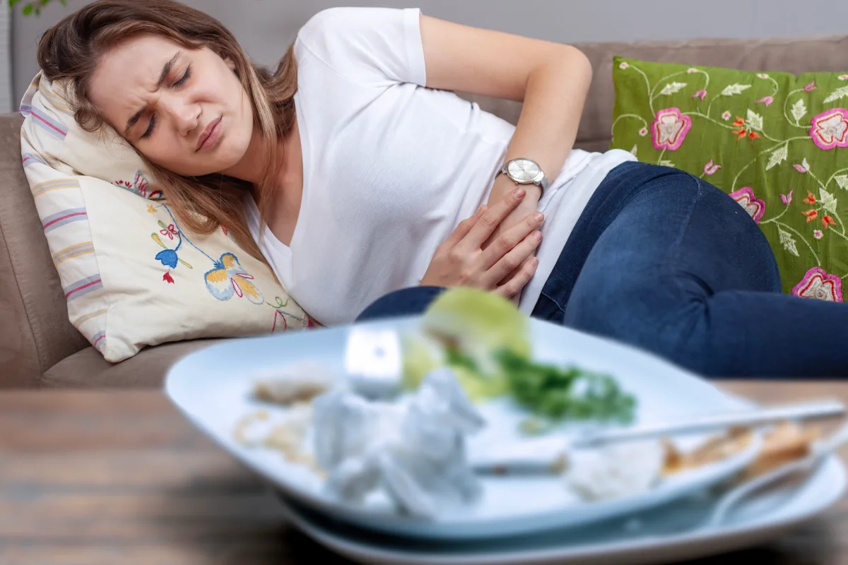 Una mujer joven se sostiene el estómago por dolor debido a una intoxicación alimentaria