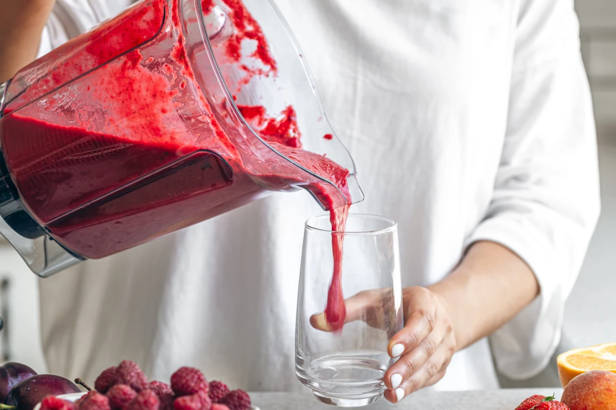 Una mujer vierte un batido de una licuadora en un vaso.