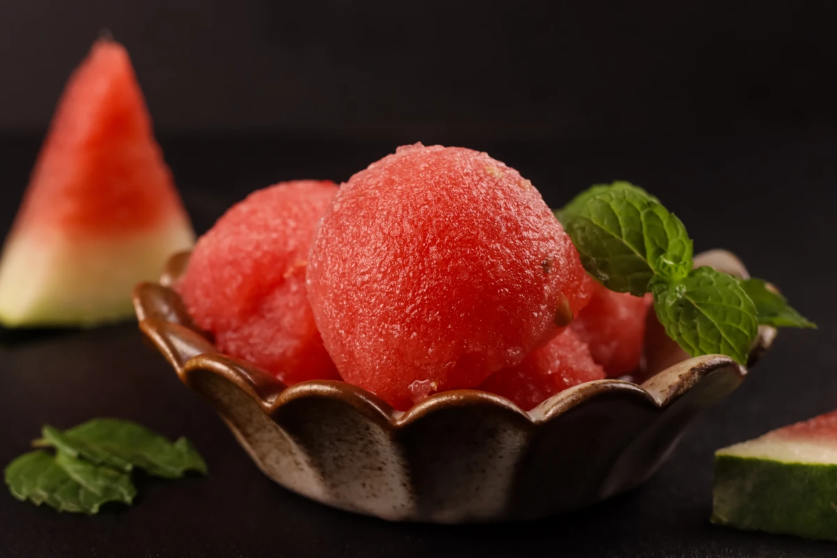 Cucharadas caseras de sorbete de sandía en un tazón, decorado con hojas de menta.