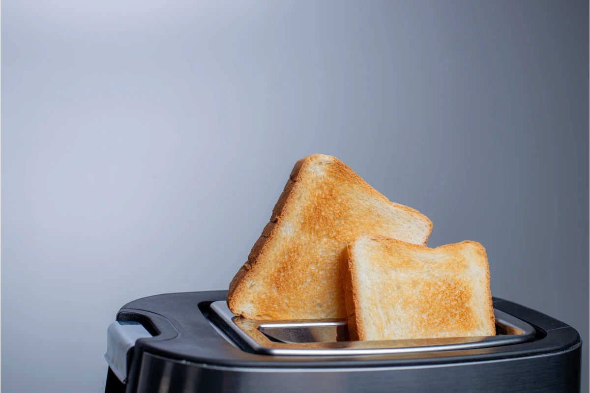 Tostadora moderna con rebanadas de pan crujiente sobre mesa blanca