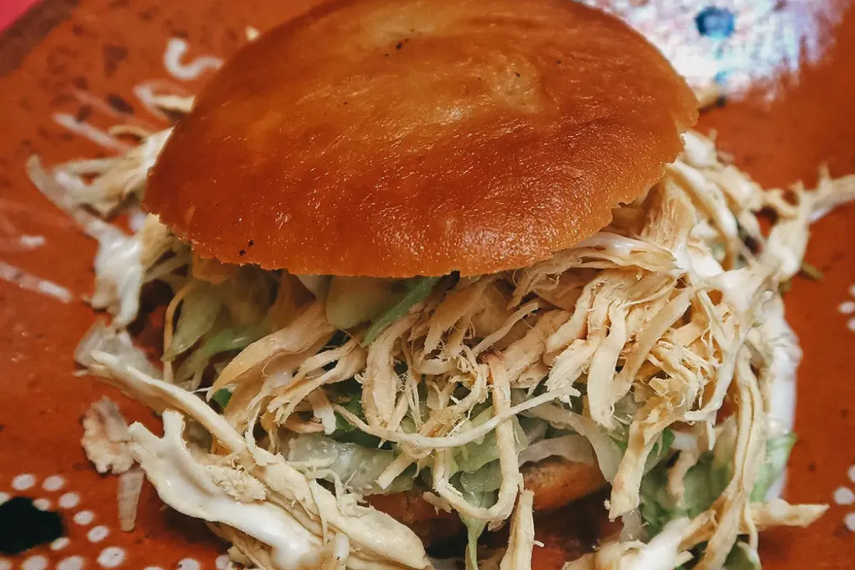 Un plato de barro sostiene una pelona poblana, un plan relleno de carne con lechuga, frijoles y crema