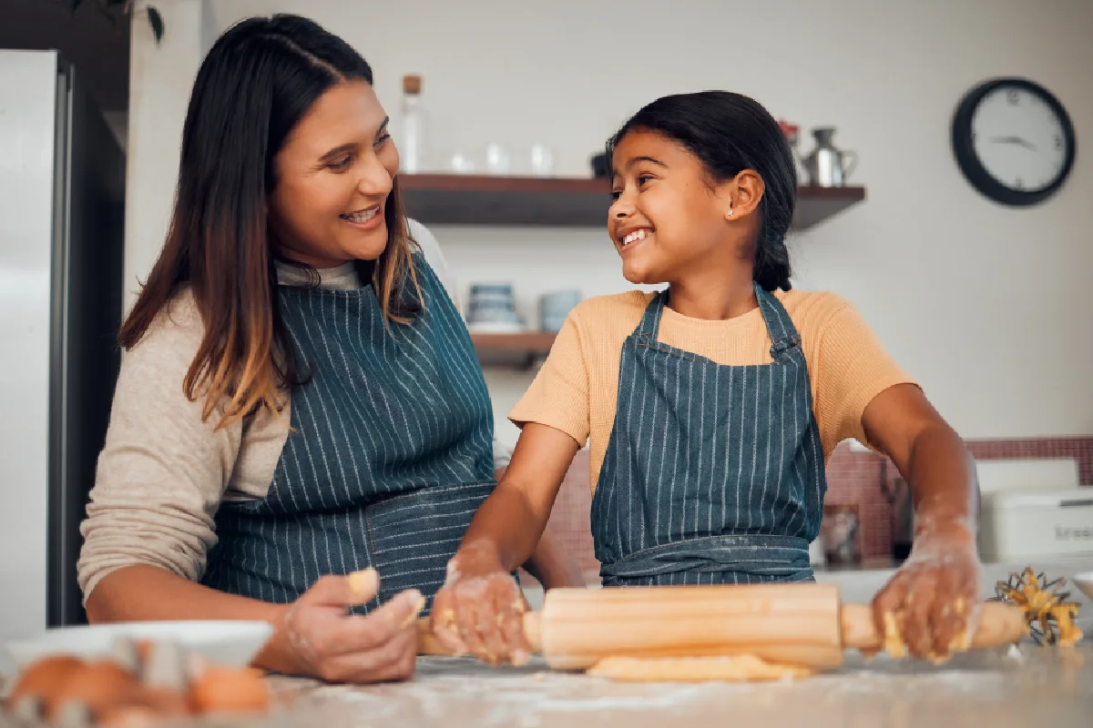 Familia, madre y niña aprendiendo a hornear en la cocina, a relacionarse y a divertirse. La comida, la educación para cocinar y la madre enseñando a los niños al cocinero cómo hacer deliciosa pastelería, sonriendo y disfrutando del tiempo de calidad juntos.
