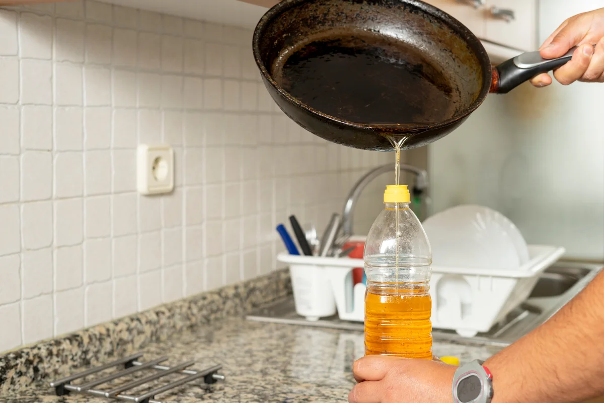 Hombre colocando aceite comestible reciclado de una sartén en una botella de plástico en su cocina.