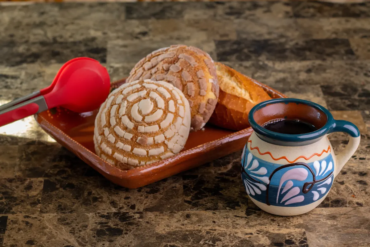 Café caliente mexicano tradicional servido con una variedad de pan dulce en un mostrador