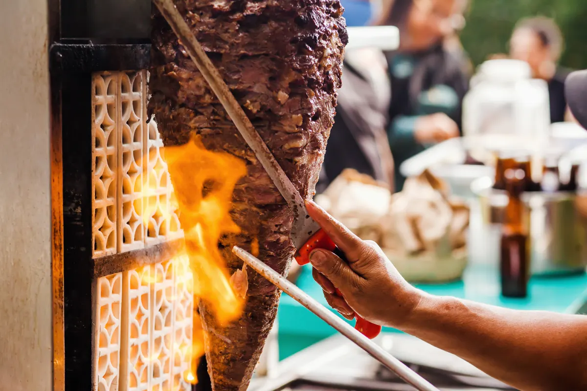 Detalle del trompo al pastor siendo cortado por un taquero