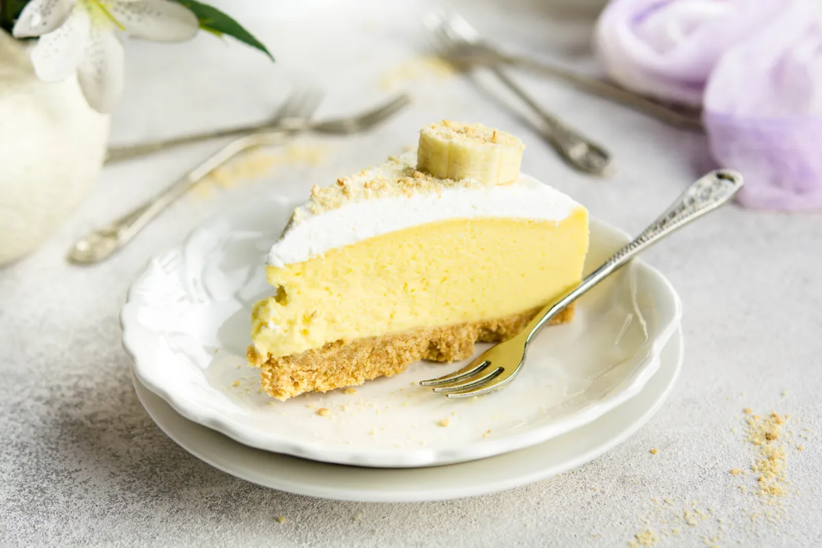 Sobre un plato blanco está servida una rebanada de cheesecake de plátano