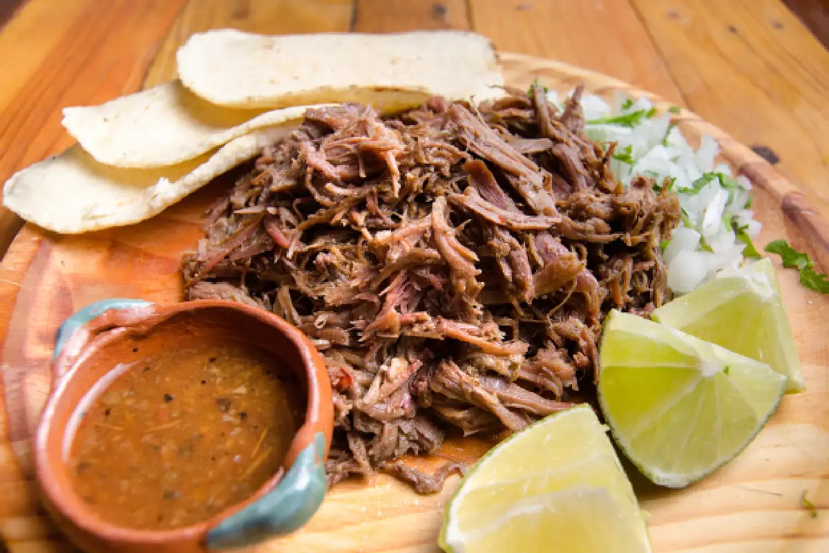 Carne de barbacoa sobre una madera con tortillas y salsa.
