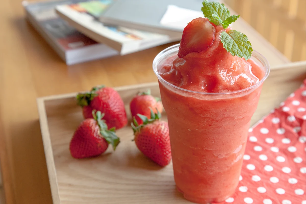 Un vaso con frappe de fresa y fresas frescas a un costado