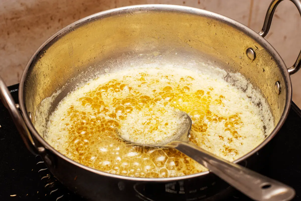 Primer plano de un proceso tradicional de hacer ghee en casa a partir de leche fresca de vaca, mostrando la rica textura dorada de la mantequilla clarificada pura.