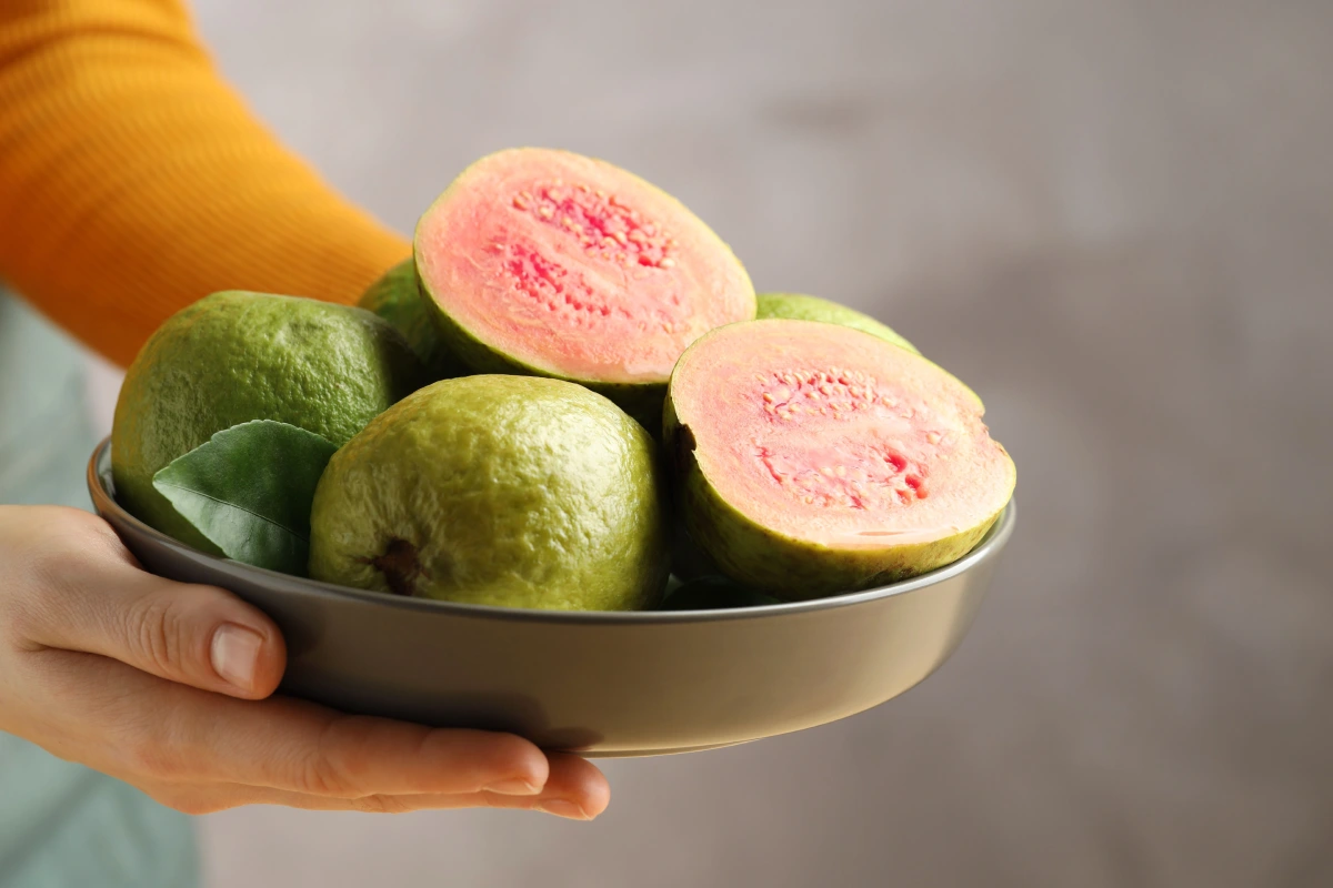 Mujer con el tazón de frutas frescas de la guayaba en el fondo gris borroso, primer plano. 
