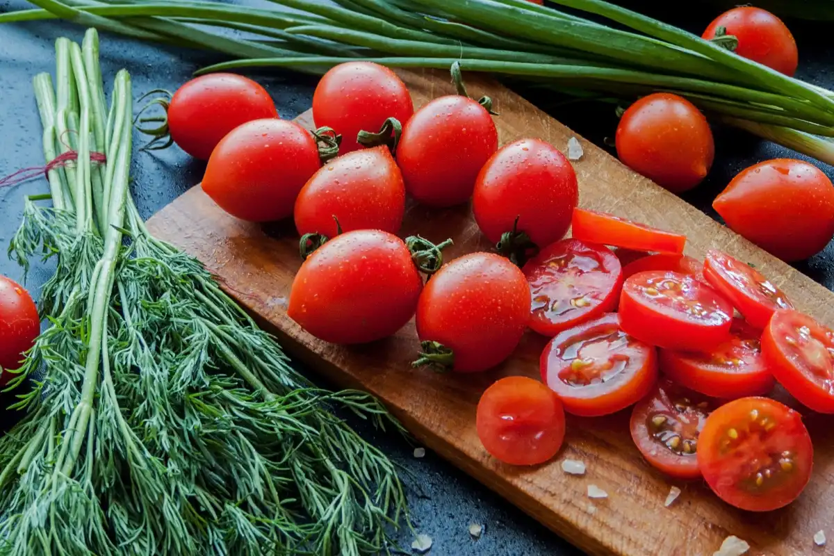 Tomates cherry rojos frescos con hierbas y puerro rociado con sal marina en la tabla de madera en la mesa, vista superior de verduras cubiertas con gotas.