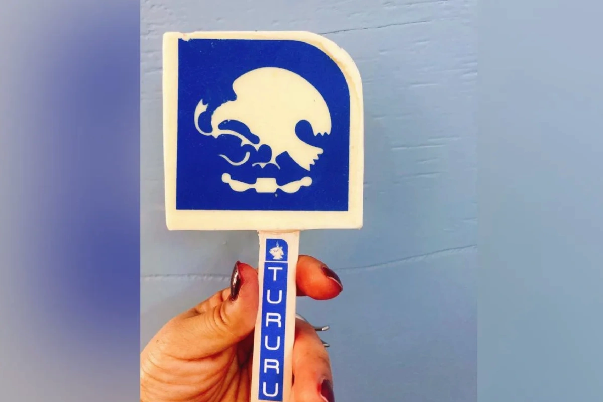 Una mano sostiene una paleta de hielo en forma de señalamiento del metro