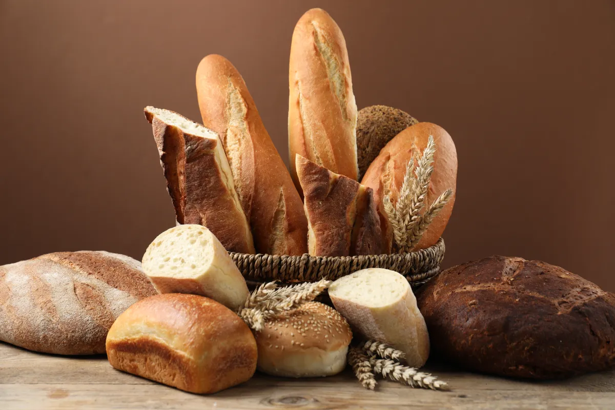 Diferentes tipos de panes en cesta de mimbre en mesa de madera contra fondo marrón, primer plano