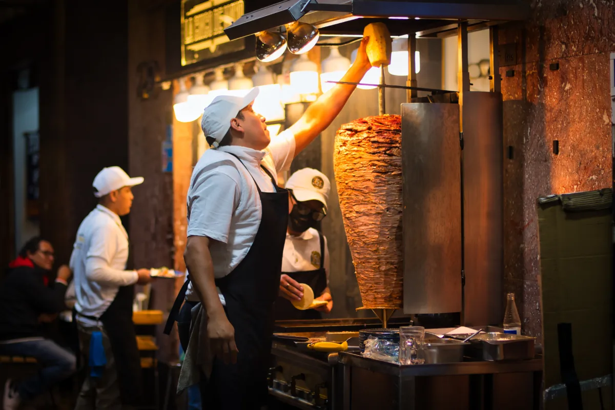 Taquero mexicano mexicano coloca la piña al trompo de pastor por la noche en un restaurante de tacos.