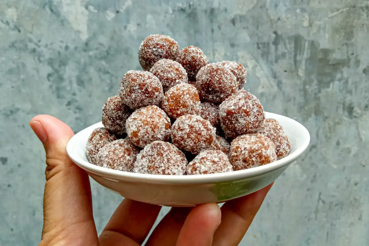 Un plato blanco es sostenido con una mano con bolitas de tamarindo con azúcar