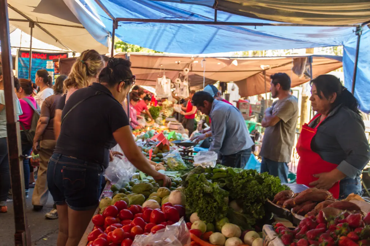 Personas comprando en un puesto de verduras que está al interior de un tianguis