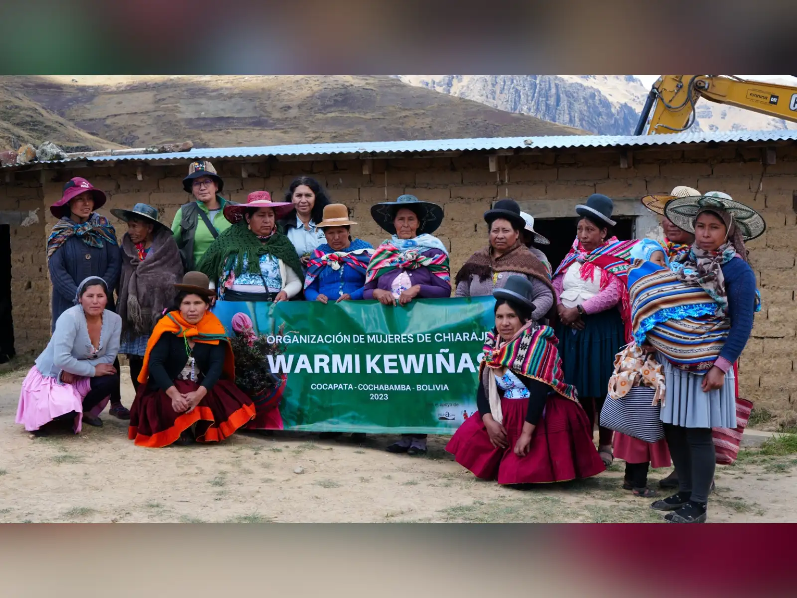 Grupo de mujeres posando para la fotografía rondeando una manta verde con el nomrbe de la organización 