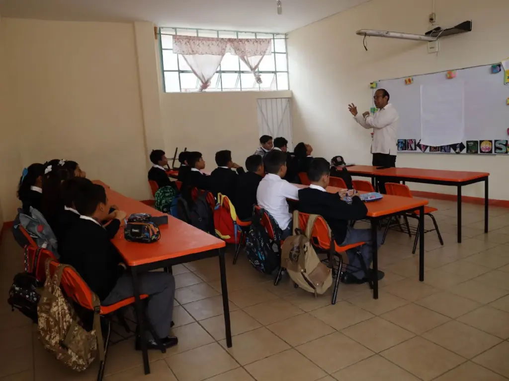 Salón de clases con niños y niñas y un maestro al frente del pizarrón