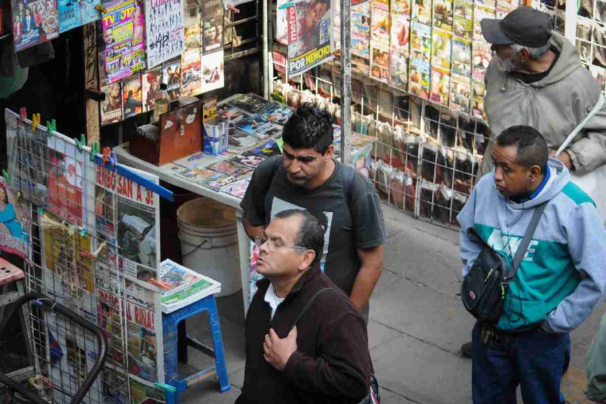 Personas leyendo periódicos colgados en un puesto 