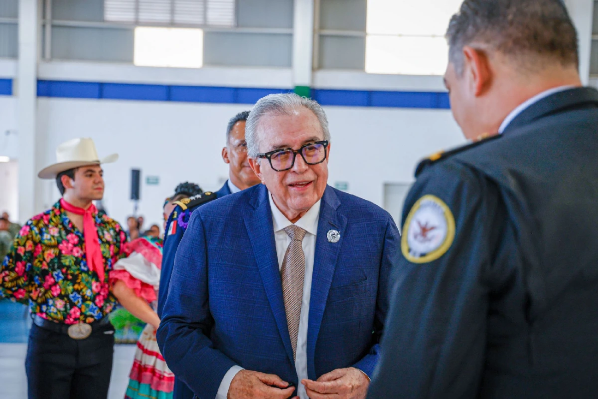 Rubén Rocha Moya de traje azul viendo de frente a un elemento del Ejército
