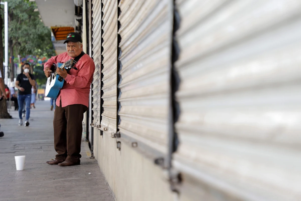 Señor toca la guitarra frente a negocios cerrados en Sinaloa