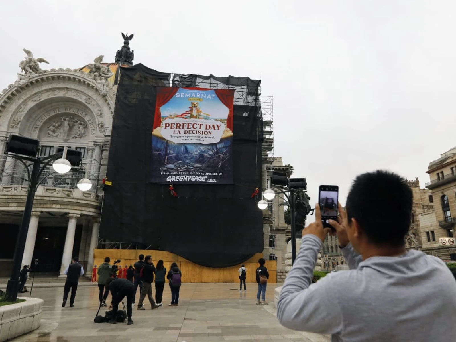 Una persona fotografía manifestacion de greenpeace en palacio de bellas artes