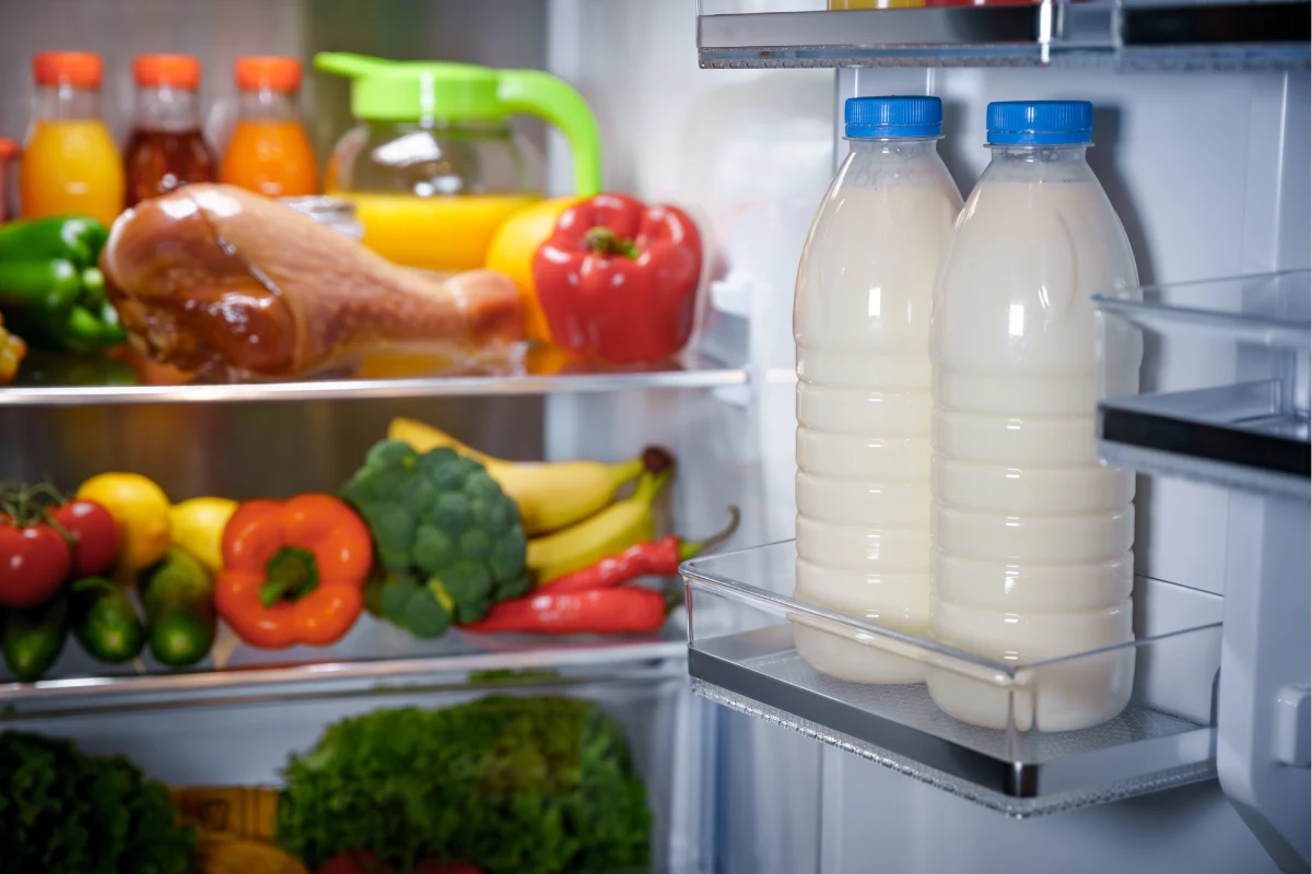Interior de un refrigerador, en la puerta hay dos litros de leche y en el interior frutas y verduras.