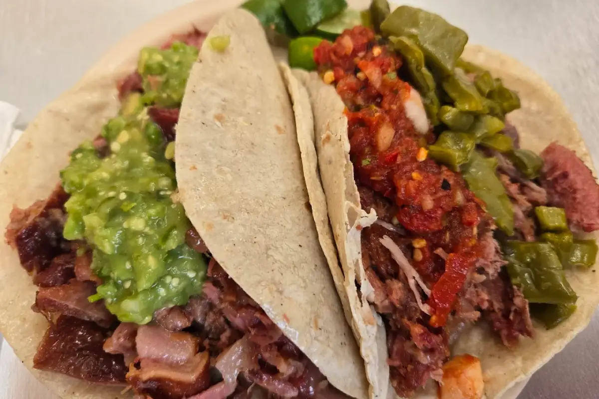 Tacos de carnitas servidos con doble tortilla y salsa roja y verde.