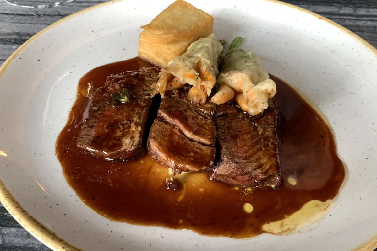 Filete de res de Sonora con flores de calabaza con una reducción de mole de olla y mil hojas de papa.