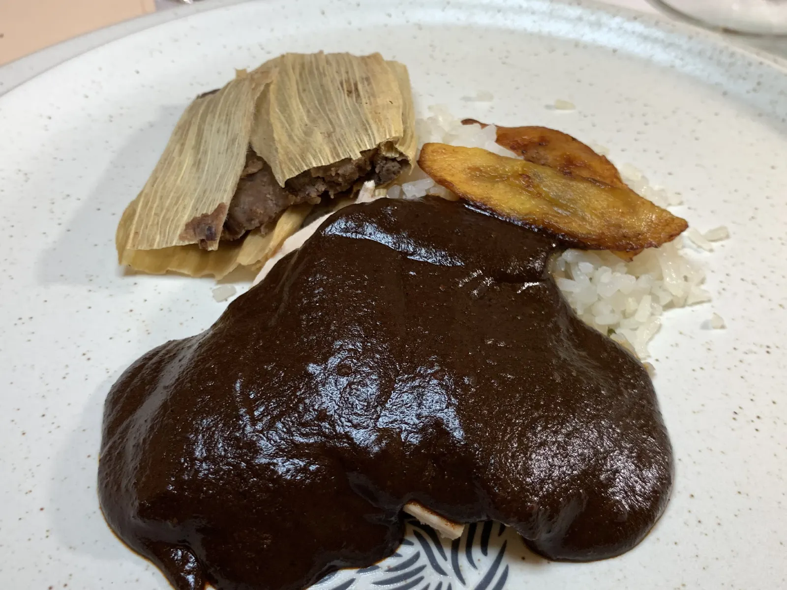 Mole servido en un plato blanco y lo acompaña un tamal de frijol y arroz blanco
