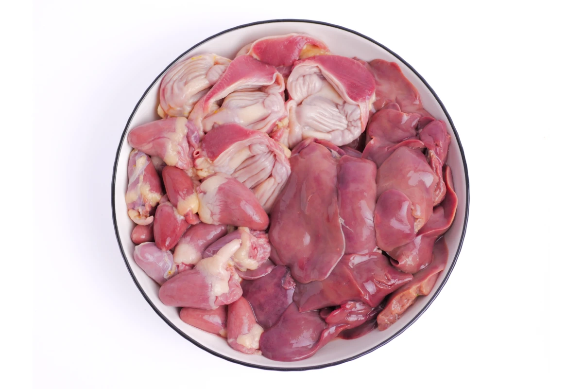 Hígado de pollo limpio, molleja y corazón cuidadosamente dispuestos en un plato blanco, fresco y listo para ser cocinado en un delicioso plato.