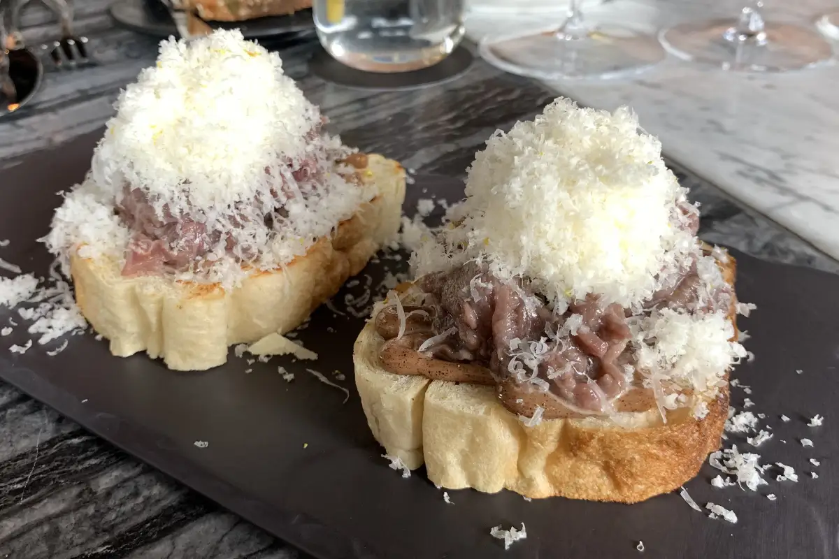Sobre un plato negro está una tapa de pan con filete en tártara