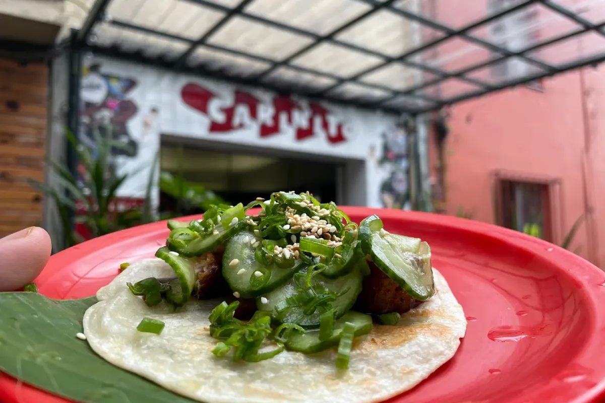 Sobre una tortilla de harina está servido un tacos con pepino, cebollin y ajonjoli