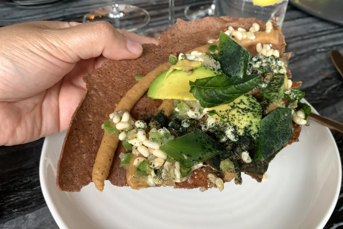 Una manos sostiene una tortilla que contiene aguacate, haba