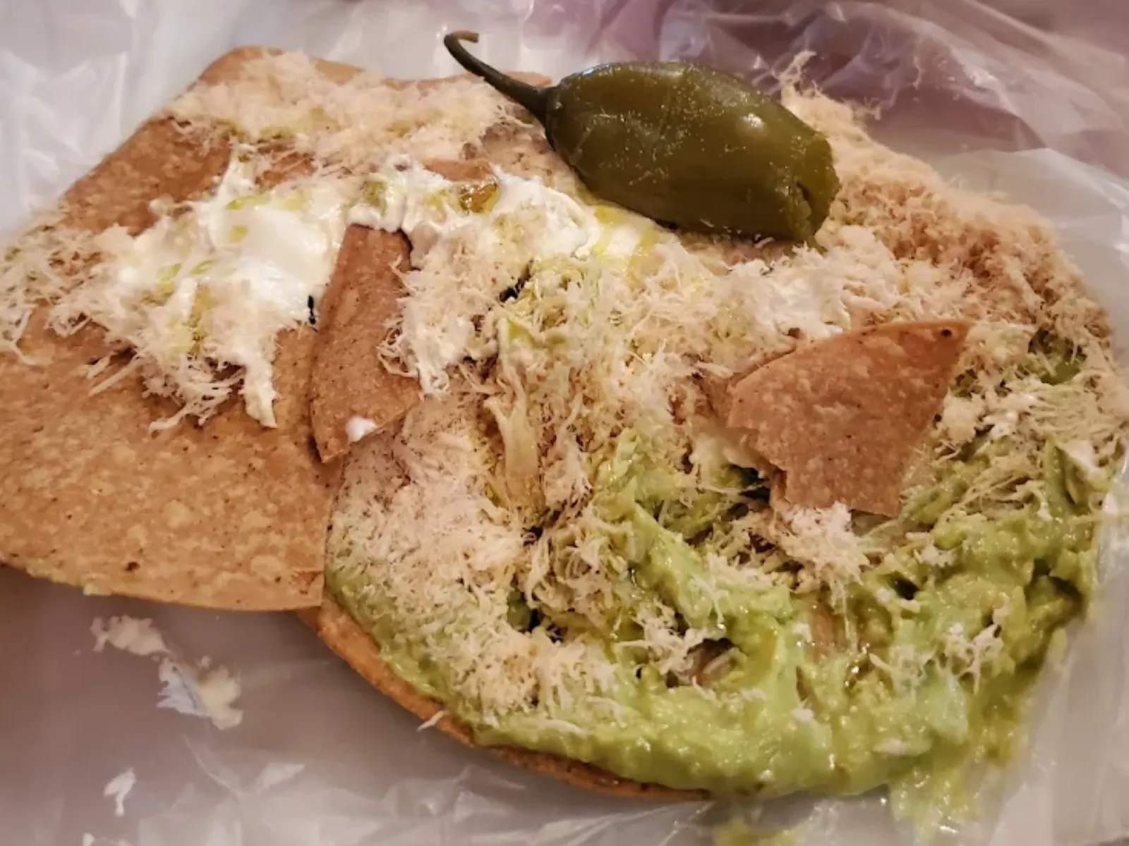 Una tostada Siberia con pollo y aguacate, junto con un chile en escabeche