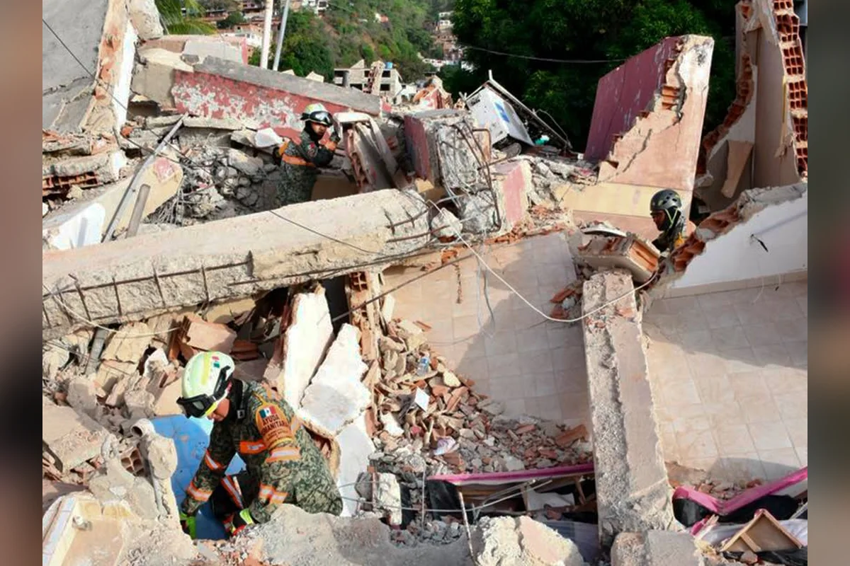 Un equipo de búsqueda y rescate mexicano, que incluye tres rescatistas con equipo protector y un perro de rescate, inspecciona los escombros de un edificio de varios pisos que ha colapsado. Un rescatista en primer plano lleva un brazalete de "Ayuda Humanitaria" de México. El perro busca entre bloques de concreto y baldosas expuestas. La escena captura la devastación del colapso con una ladera de la ciudad visible al fondo. Barras de desenfoque horizontales enmarcan la imagen.