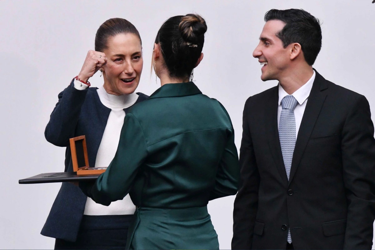 Sheinbuam con el puño en alto en señal de festejo entregando un premio a Katia Itzel, que usa un vestido verde y está de espaldas.