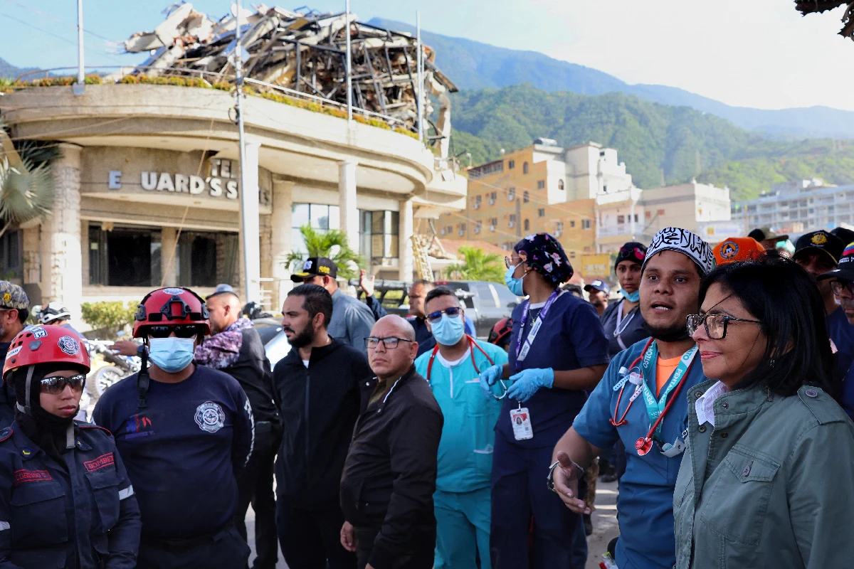 Un edificio derrumbo de fondo con la presidenta encargada de venezuela y otras paeronas a su alrededor 