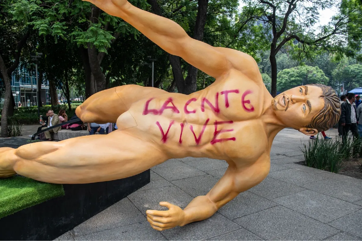Estatua de un futbolista sin ropa derriba y con pintura que dice "LA CNTE VIVE"