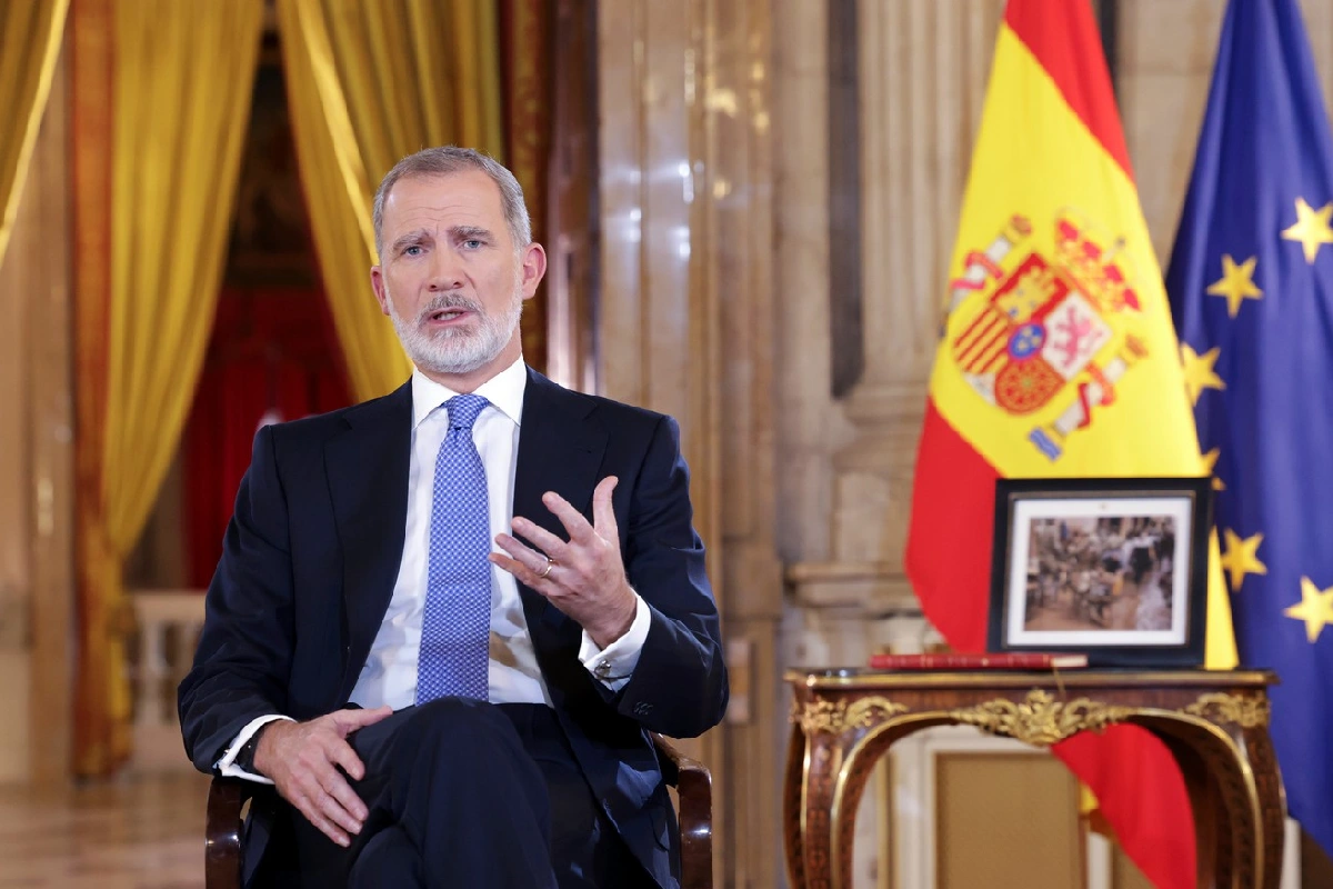 Rey de España sentado con la bandera de españa y la únión europea detrás de él