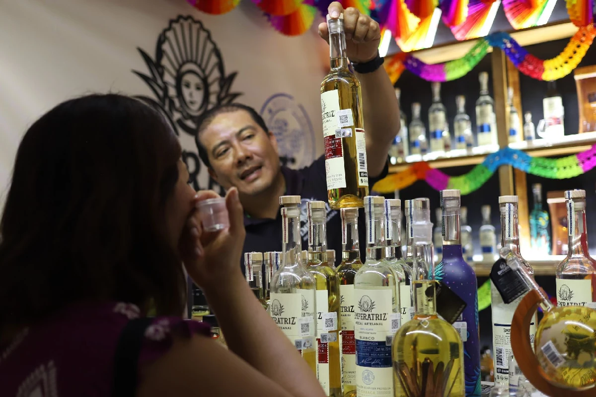 Un vendedor muesta una botella de mezcal a una clienta