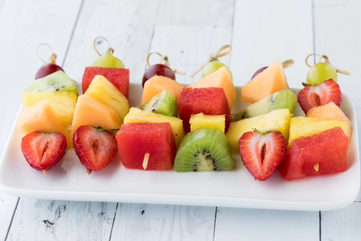 Brochetas de fruta fresca sobre una bandeja sobre una mesa blanca de madera.