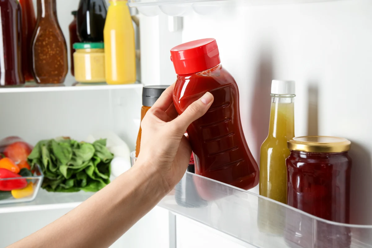 Mano de mujer agarra un bote de catsup que está al interior de un refrigerador