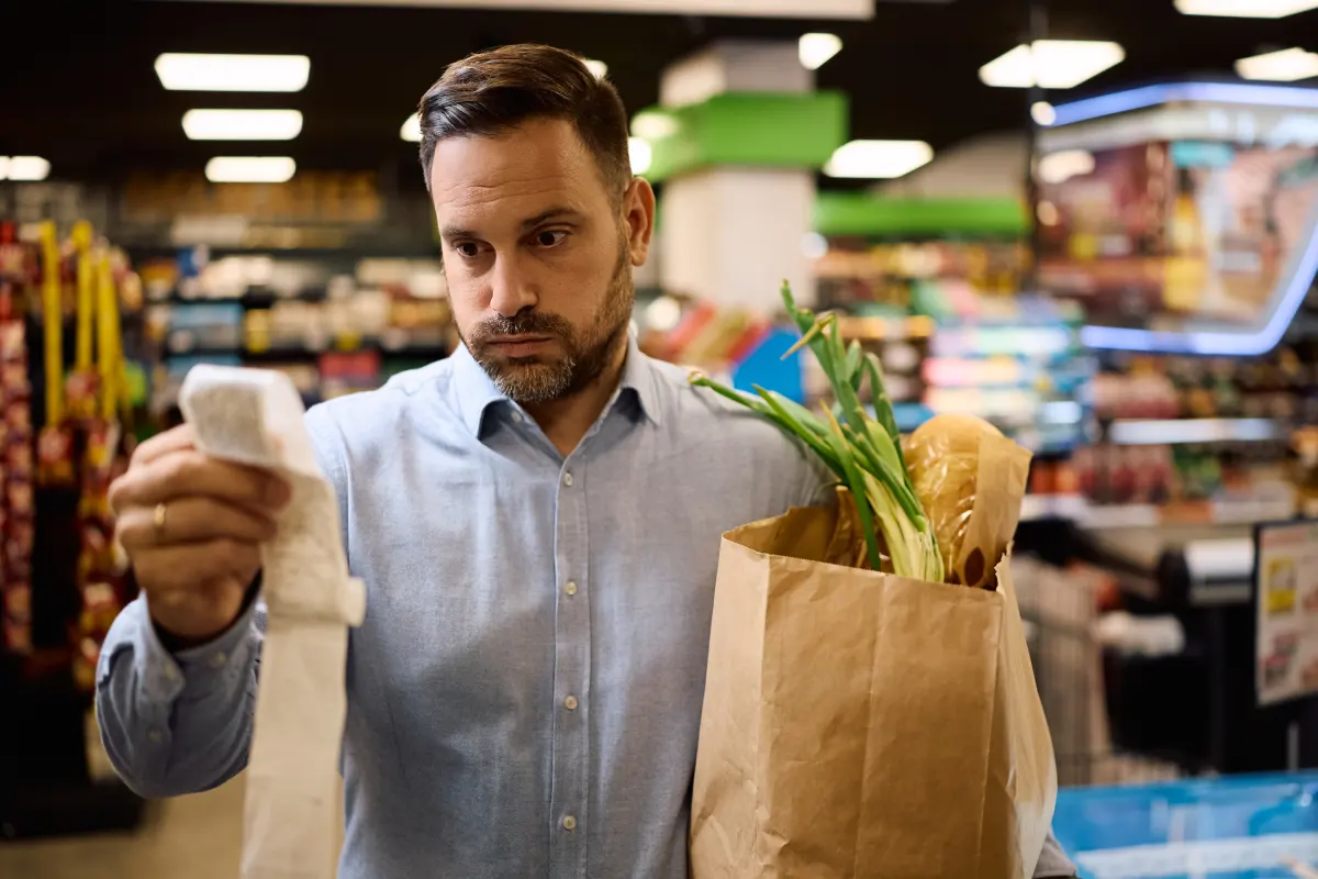 Hombre preocupado que comprueba la cuenta después de comprar comestibles en el supermercado