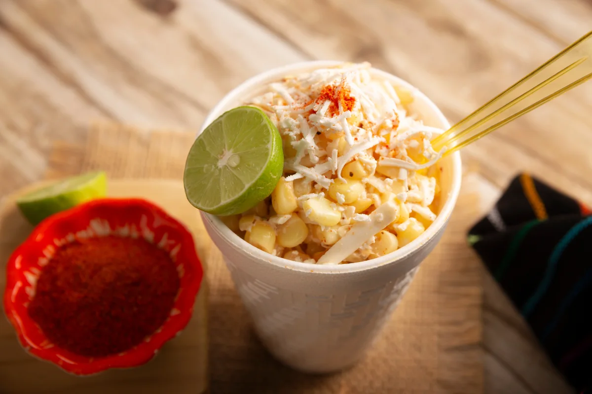 Granos de elote con queso y mayonesa servidos en un vaso de unicel