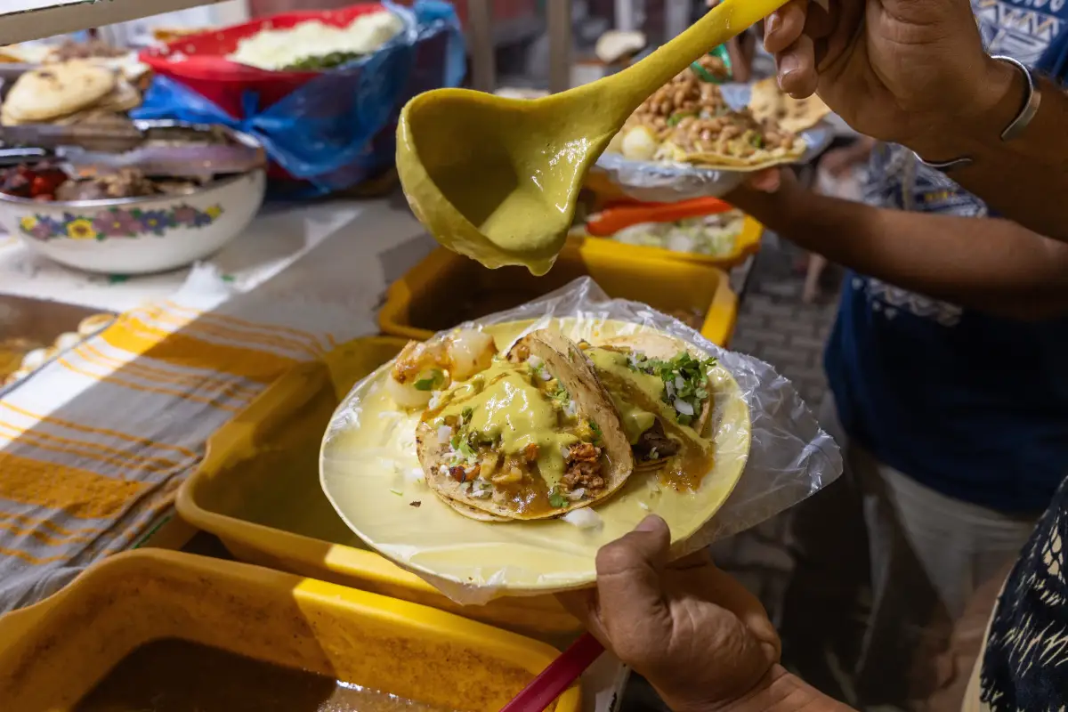 Hombre vierte salsa verde en unos tacos