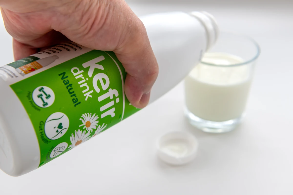 Una persona vierte yogur de kéfir de una botella en un tazón de fruta